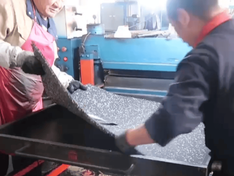 Quality control engineer inspecting a roll of black rubber gym flooring in a factory setting
